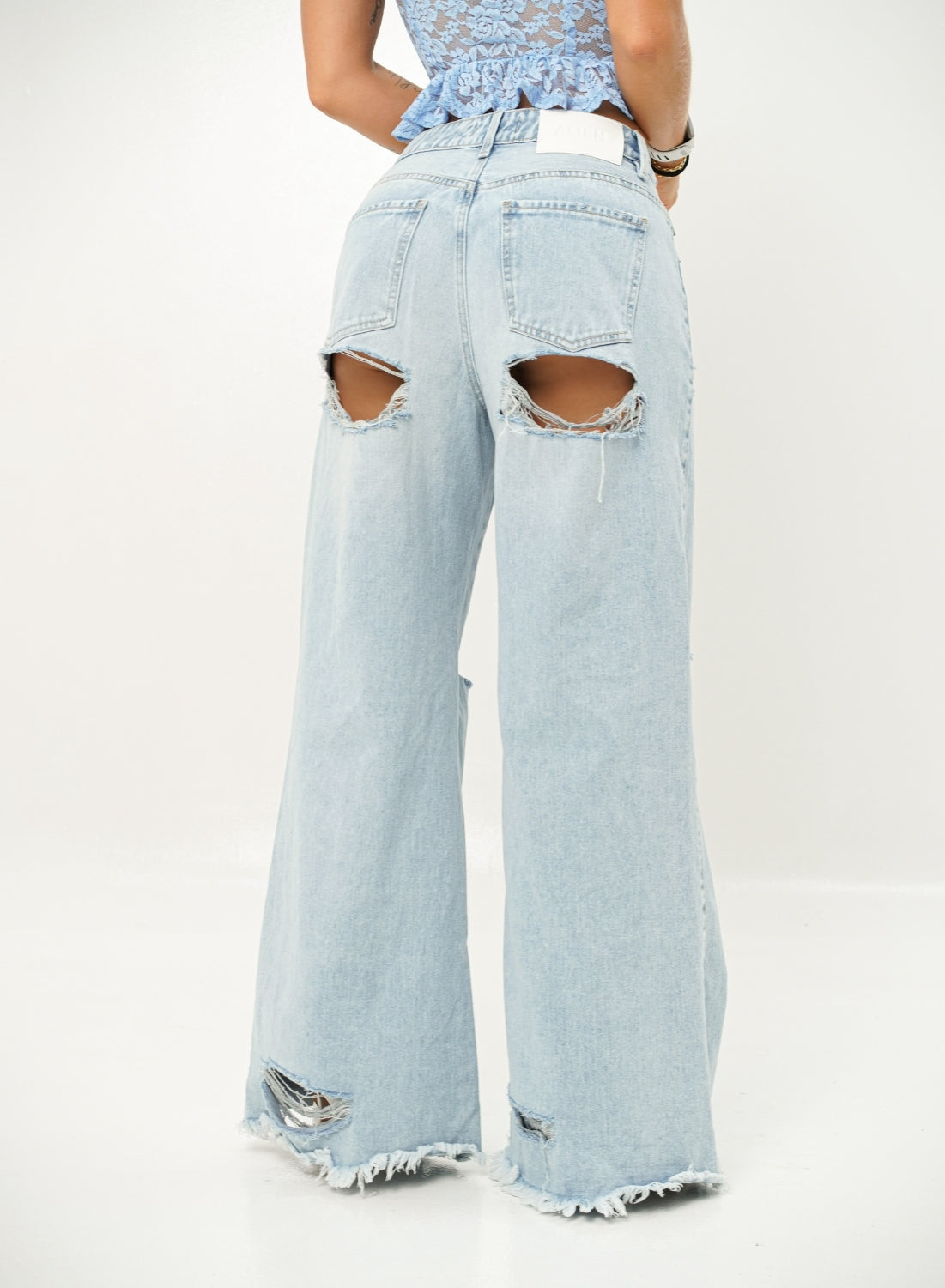 Woman wearing a light blue lace top and ripped denim jeans on a white background