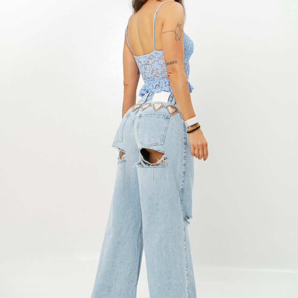 Woman wearing a light blue lace top and ripped denim jeans on a white background