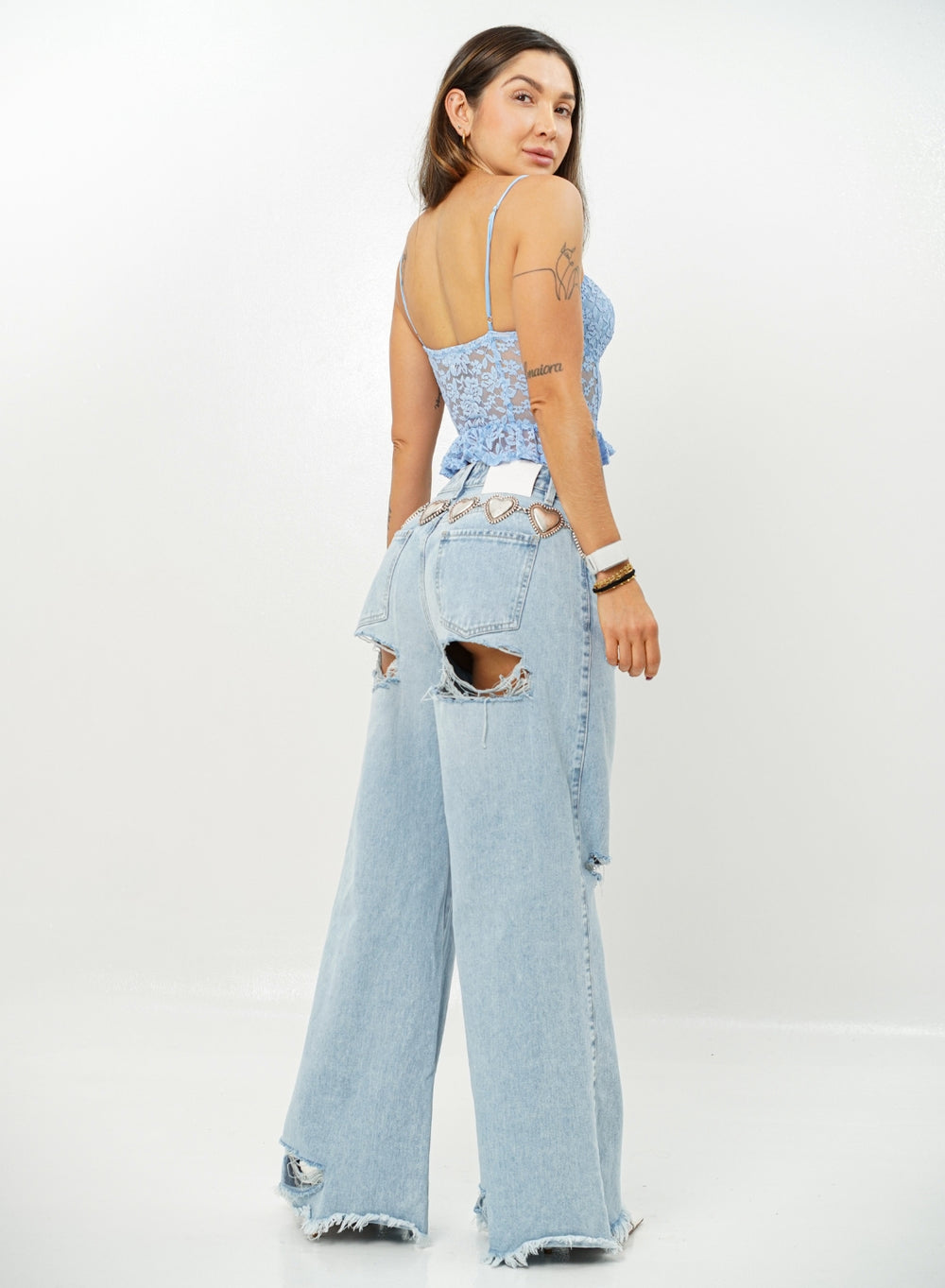 Woman wearing a light blue lace top and ripped denim jeans on a white background