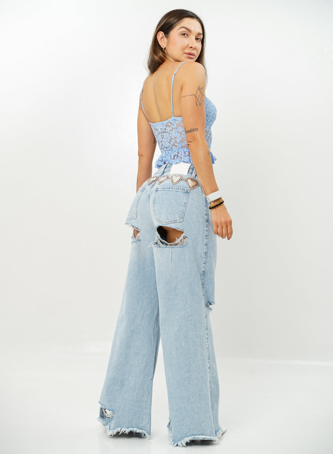 Woman wearing a light blue lace top and ripped denim jeans on a white background