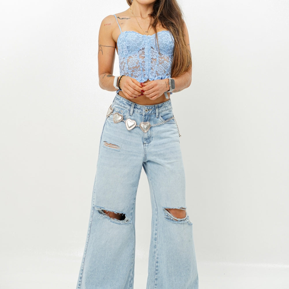 Woman wearing a light blue lace top and ripped denim jeans on a white background