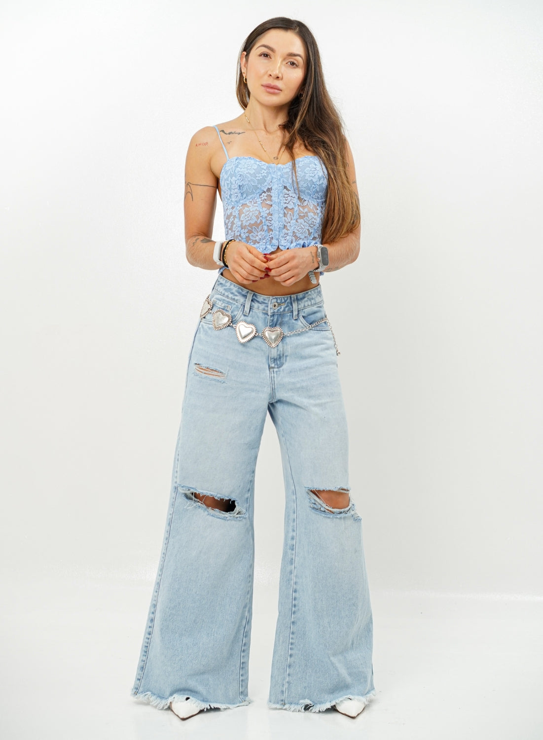 Woman wearing a light blue lace top and ripped denim jeans on a white background